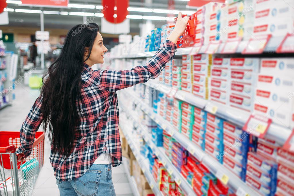 Young woman buying toothpaste in supermarket. Female customer on  shopping in hypermarket, department of personal care products