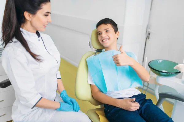 女牙医和小男孩在牙科椅显示竖起大拇指 儿科牙科 儿童口腔医学 — 图库照片