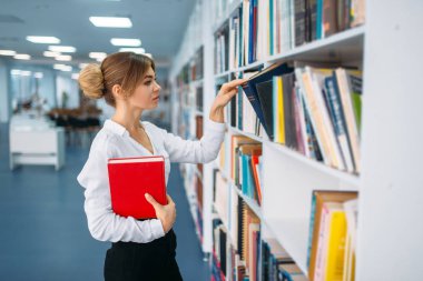 Genç kadın raf kitaplığındaki kitap bakarak. Okuma odası, bilgi deposu içinde kadın kişi