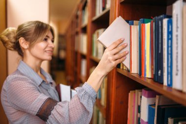 Genç kadın kitap raf üniversite kitaplığında alır. Kadın kişisel bilgi deposu olarak