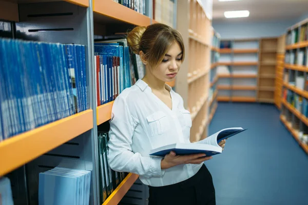 Çekici kız öğrencinin Üniversite Kütüphanesi içinde Bookshelf kitap okumak. Okuma odası, bilgi deposu olarak genç kadın