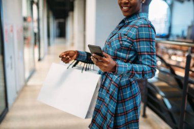 Siyah kadın kişi ile telefon ve alışveriş merkezinde alışveriş torbaları. Alışverişkoliğin Giyim Mağazası, tüketim yaşam tarzı, moda