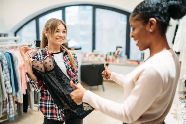 İki kadın seçme samimi giyim, alışveriş. Shopaholics Giyim Mağazası, tüketim yaşam tarzı, moda, iç çamaşırı bölümünde kadın alışveriş