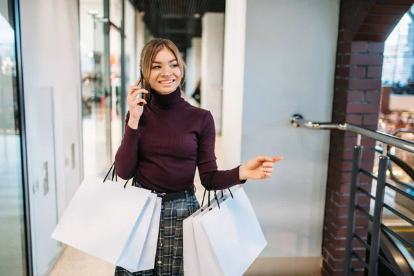 Female customer with shopping bag talking by phone in mall. Shopaholic in clothing store, consumerism lifestyle, fashion, attractive lady purchasing in shop