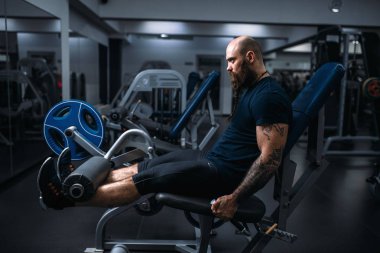Kas atlet spor salonunda eğitim egzersiz makinesi, bacaklarına eğitiyor. Sakallı adam Spor Kulübü, sağlıklı bir yaşam tarzı olarak çalışma