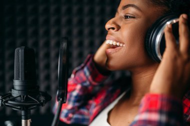 Female singer in headphones songs in audio recording studio. Musician listens composition, professional music clipart