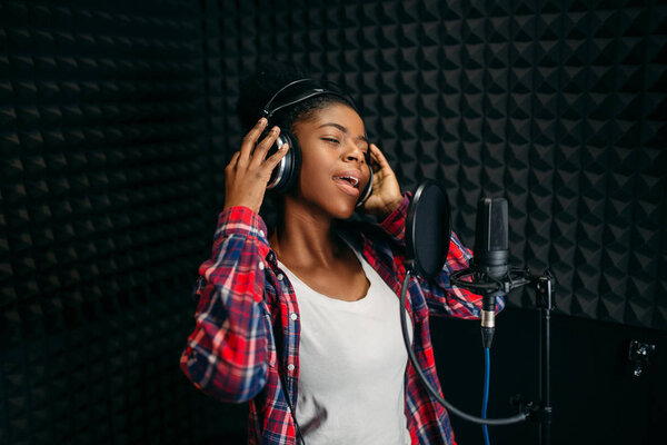 Female singer in headphones songs in audio recording studio. Musician listens composition, professional music