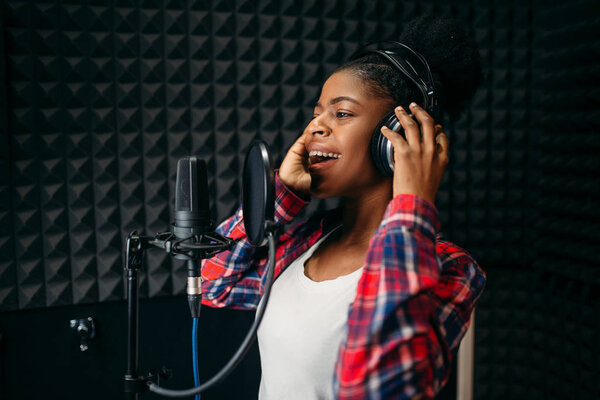 Female singer in headphones songs in audio recording studio. Musician  listens composition, professional music mixing