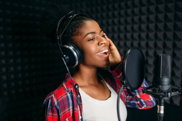 Female singer in headphones songs in audio recording studio. Musician listens composition, professional music mixing