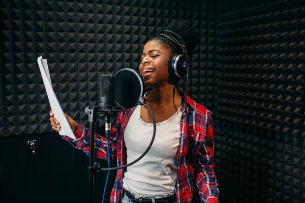 Young woman in headphones songs in audio recording studio. Musician listens composition, professional music mixing