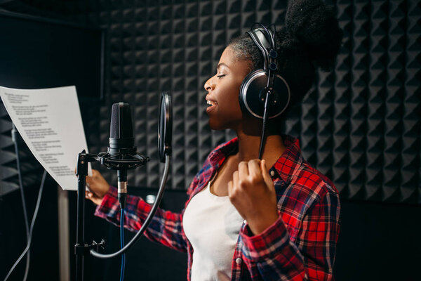 Young woman in headphones songs in audio recording studio. Musician  listens composition, professional music mixing