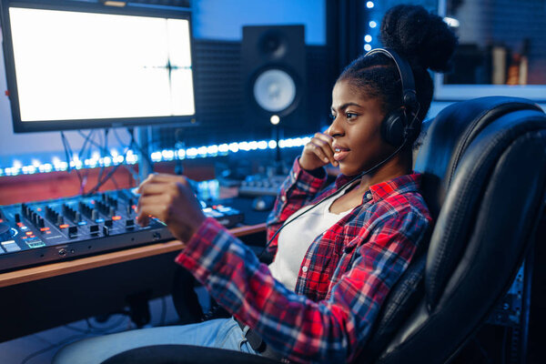 Female performer in headphones at the monitor in audio recording studio. Sound engineer at the mixer, professional music mixing