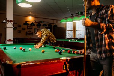 İki erkek Bilardo oyuncular cues pozlar renkli topları ile masada ile Bilardo. Erkek spor bar Amerikan pool oyunu oynar