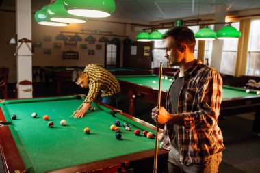 İki erkek Bilardo oyuncular cues pozlar renkli topları ile masada ile Bilardo. Erkek spor bar Amerikan pool oyunu oynar