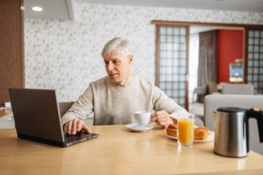 Neşeli yetişkin adam evde dizüstü kahvaltı vardır. Kot olgun erkek kişi mutfakta rahatlayın