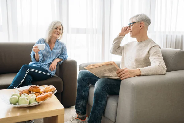 成人爱情夫妇早上在家 男人看报纸 女人喝咖啡 成熟的丈夫和妻子坐在沙发上 幸福的家庭 — 图库照片