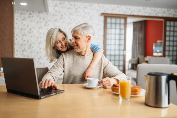 陽気な大人の恋愛カップル自宅の朝食 成熟した夫と妻の幸せな家庭のキッチンでノート パソコンで — ストック写真