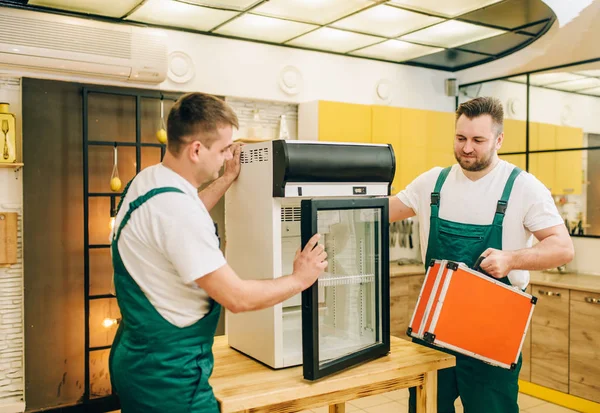 Male workers in uniform repair refrigerator at home. Repairing of fridge occupation, professional service