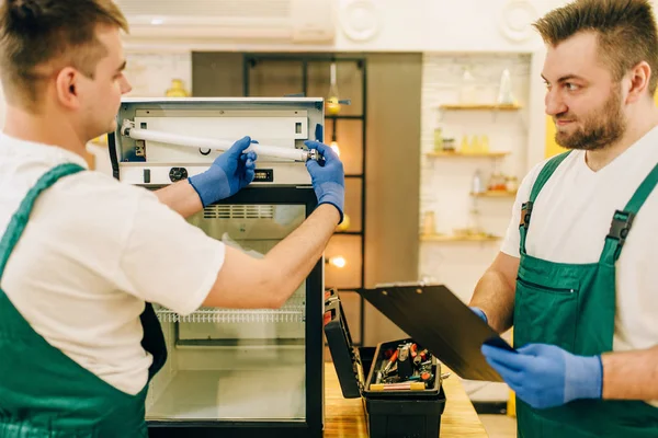 Two technicians in uniform repair refrigerator at home. Repairing of fridge occupation, professional service