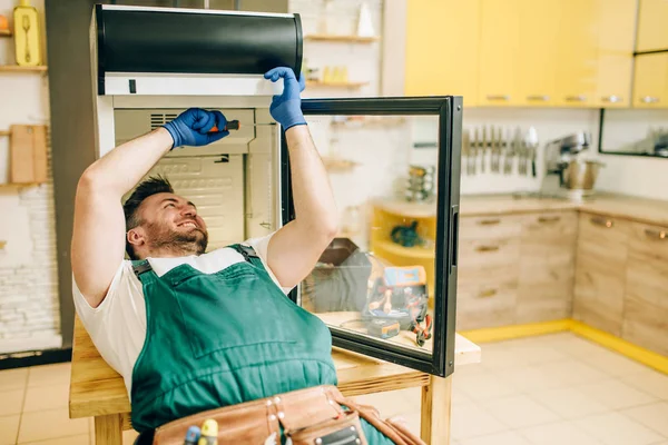 Worker in gloves and uniform repair refrigerator at home. Repairing of fridge occupation, professional service