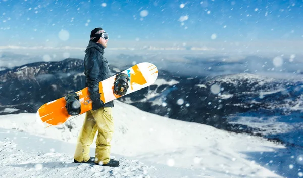 Erkek snowboard ile tahta bir karlı dağın tepesinde duruyor. Snowboard aşırı kış bir spordur. Adam önce tehlikeli downhill snowboard ile