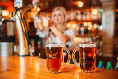 Tezgahta taze bira iki bardak, seksi garson barda bir kupa içine köpüklü içecek döker. Geleneksel stil elbise çekici şekiller ile Octoberfest barmaid