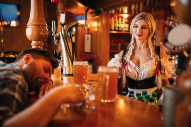 Barda bira kupaları ile tezgahta uyuyan sarhoş adam, arka planda güzel garson, oktoberfest tatil. Erkek kişi barda içme, geleneksel retro tarzında barmaid