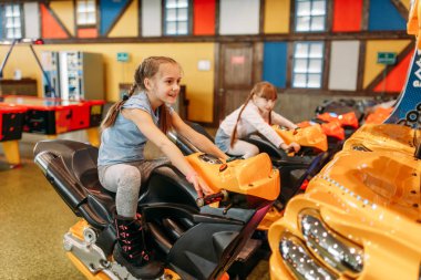 İki küçük kız oyun makinesi, çocuk eğlence merkezi çalış. Heyecanlı Childs'ın kapalı oyun alanında eğleniyor. Motosiklet, eğlence merkezi oynayan çocuklar