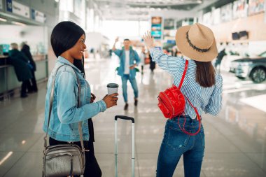 İki kadın turist havaalanında bir arkadaşıyla buluşuyor. Hava terminalinde bagaj, mutlu yolculuk, yaz seyahati olan yolcular