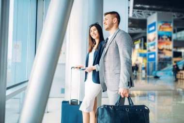 Havaalanında bagajı olan business class yolcuları, arka görüş. İşadamı ve iş kadını hava terminalinde, müzakere gezisi