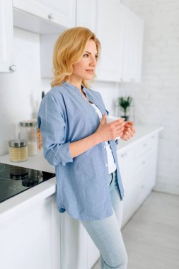 Woman standing on the kitchen with snow-white interior. Female person at home in the morning, healthy nutrition and lifestyle