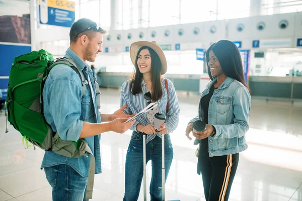 Three tourists with luggage waiting for departure in airport. Passengers with baggage in air terminal, happy journey, summer travel