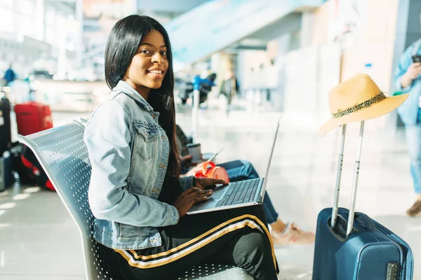 带着笔记本电脑的女游客在机场等候出发 旅客在航空站携带行李 黑人女士快乐旅程 — 图库照片