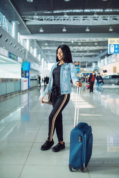 Black female tourist with suitcase and phone waiting for departure in international airport. Passenger with baggage in air terminal, happy journey sexy lady, summer travel of happy woman