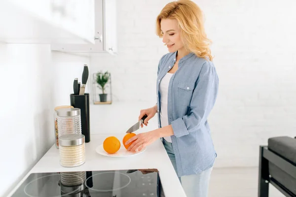 オレンジを準備ナイフを持つ幸せな女性 キッチンで朝食 朝の在宅女性 健康的な栄養とライフスタイル — ストック写真