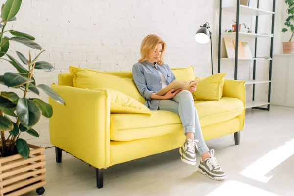 Mujer Joven Leyendo Libro Sobre Acogedor Sofá Amarillo Sala Estar —  Fotos de Stock