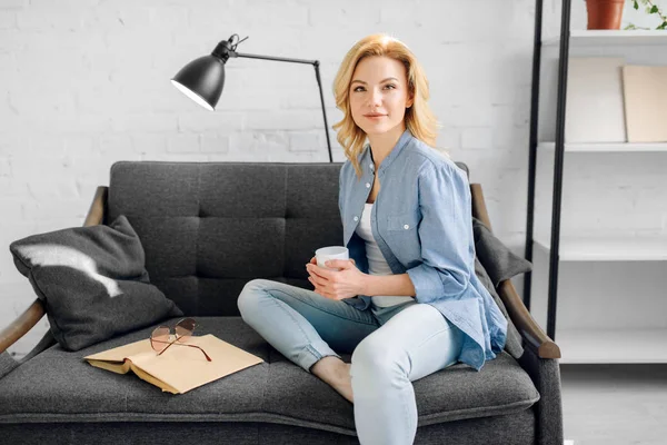 Jonge Dame Met Boek Kopje Koffie Poseert Gezellige Zwarte Bank — Stockfoto