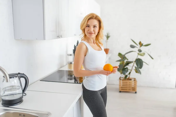 スポーティな女性はオレンジを投げる 台所にフィット朝食 朝の自宅で女性 ライフスタイル — ストック写真