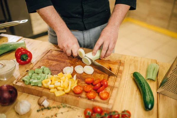 Chef hands with knife cuts mushrooms on wooden board closeup. Man cutting vegetables on counter, fresh salad cooking, kitchen interior on background. Male person chopping ingredients for lettuce