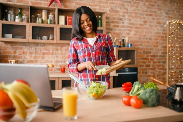 Black woman cooking breakfast on the kitchen. African female person preparing vegetable salad at home. Healthy vegetarian lifestyle