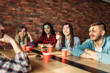 Gülümseyen arkadaşlar alın oyunu için etiket notları oynarken. Şirket kafede masada kim olduğumu oynar, insanlar karakter tahmin