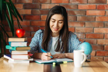 Üstte ders kitapları ve elma, arka planda tuğla duvar, bilgi kavramı ile masada oturan kız üniversite öğrencisi
