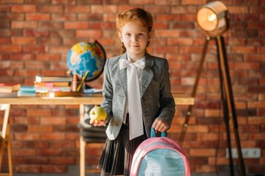 Okul çantası, yan görünümü ile sevimli kız öğrenci. Sırt çantası ile kız öğrenci, ders kitapları ile masa, backgrpund üzerinde elma ve küre, okulda genç kız