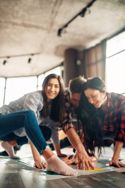 Group of students playing twister game. Youth in funny poses on the floor, entertainment for active company