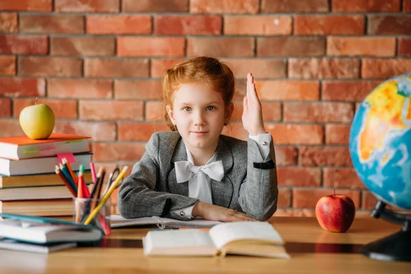 Mooi Schoolmeisje Met Verhoogde Hand Zittend Aan Tafel Met Leerboeken — Stockfoto
