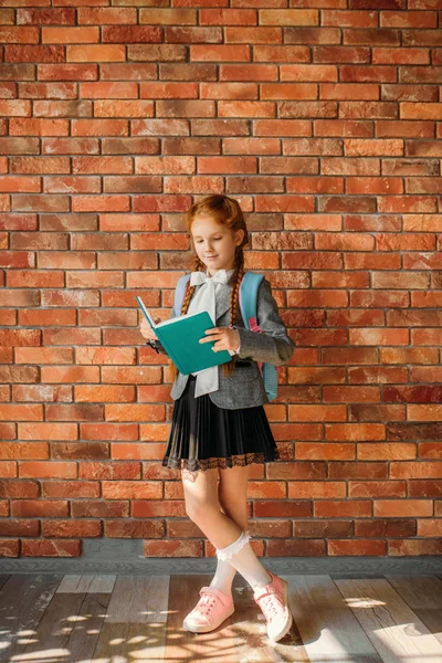 Söt Schoolgirl Med Schoolbag Läsa Lärobok Tegelvägg Bakgrunden Bedårande Kvinnlig — Stockfoto