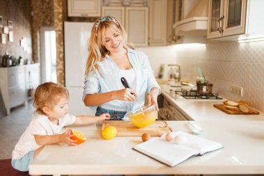 Genç Anne ve kızı bir kase meyve karıştırma. Mutfakta sevimli kadın ve küçük kız pişirme, pasta hazırlama. Mutlu aile tablo üzerinde tatlı tatlı, malzemeler hazırlar