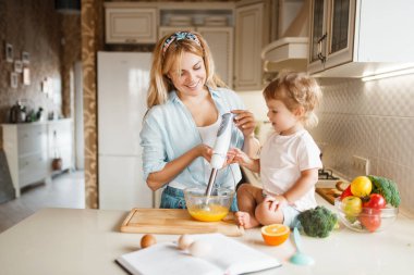 Genç Anne ve kızı bir kase bir blender ile kek için malzemeyi fırçalamak. Sevimli kadın ve küçük çocuk mutfakta yemek, pasta hazırlama. Mutlu aile tatlı tatlıyı hazırlar