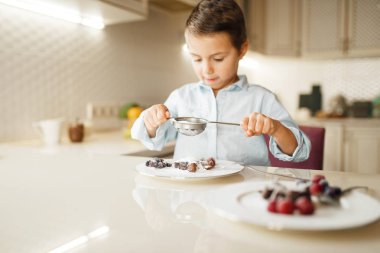 Genç çocuk doğal erimiş çikolata ile sandviç gösterir. Mutfakta yemek yapan sevimli erkek çocuk. Mutlu çocuk hazırlar ve masada tatlı tatlıları tadı