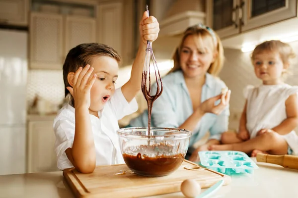 Young mother and her kids tastes fresh pastry with melted chocolate. Woman and little children cooking on the kitchen, cake preparation. Happy family eats sweet dessert
